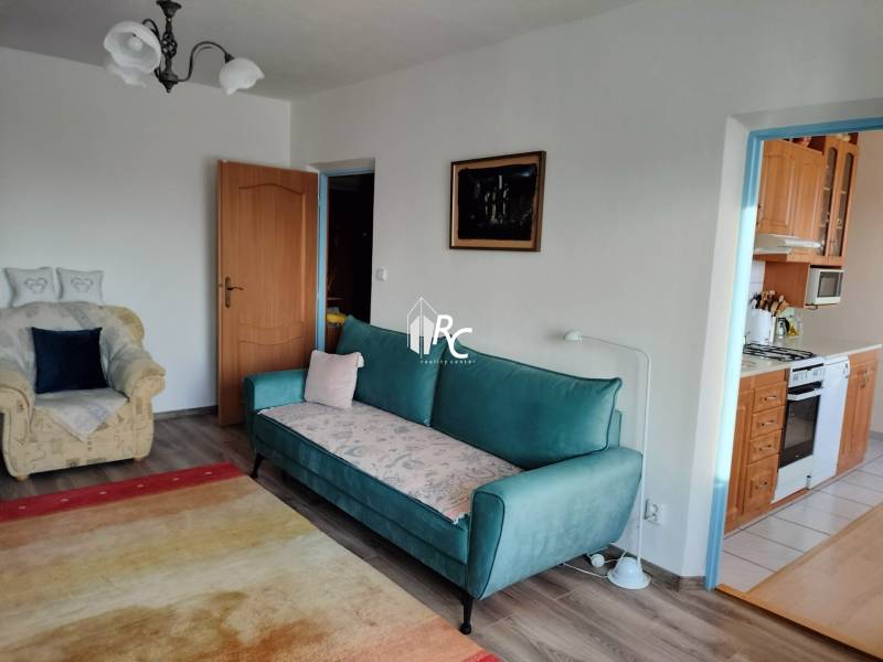 2 izbový byt na Severe - Obývacia izba v 2-izbovom byte s pohovkou a kreslom, podlaha s dreveným dekorom.