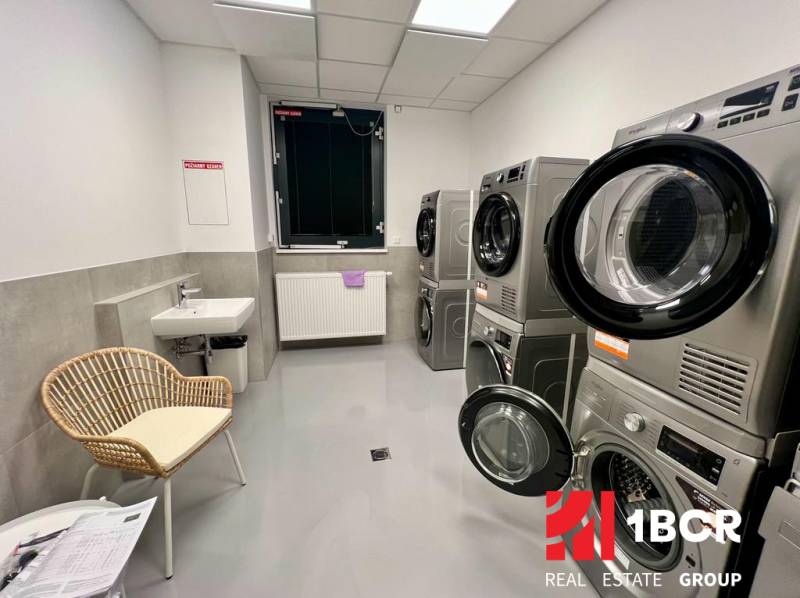 KOMPLETNE ZARIADENÝ SVETLÝ 2-IZB. BYT, NOVOSTAVBA NUPPU, HRANIČNÁ UL. - Práčovňa s práčkami, sušičkami, umývadlom a stoličkou v 2-izbovom byte.