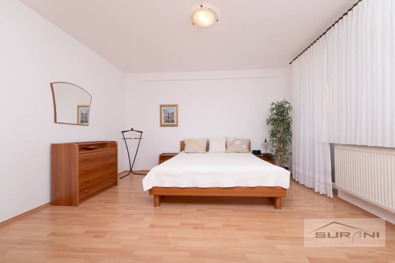 Nové v ponuke | 3-izbový byt 91 m² | 2× balkón | parkovanie | RUSTICA  - Spálňa s posteľou, komodou a podlahou s dreveným dekorom v 3-izbovom byte.