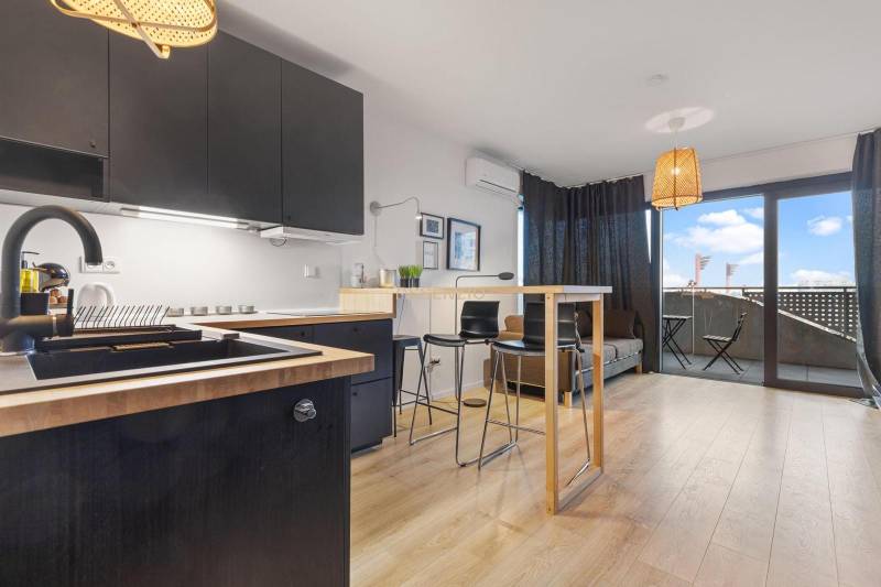 - PREDAJ - APARTMÁN - 38 m2 + 14 m2 LOGGIA - TEHELNÉ POLE - Kuchyňa s čiernymi skrinkami, barovým pultom a podlahou s dreveným dekorom v 1-izbovom byte.