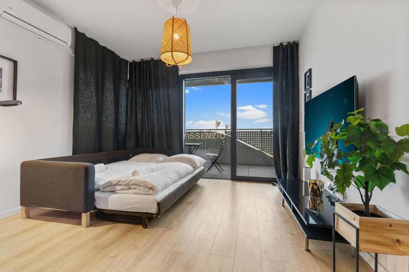 - PREDAJ - APARTMÁN - 38 m2 + 14 m2 LOGGIA - TEHELNÉ POLE - Obývacia časť v 1-izbovom byte s posteľou, podlahou s dreveným dekorom a balkónom.