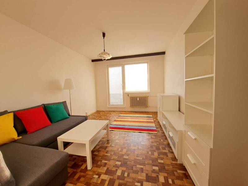 Prenájom 2-izbového bytu v Poprade na Dostojevského ul. - Obývacia izba v 2-izbovom byte s pohovkou, bielym nábytkom, pestrofarebnými vankúšmi a podlahou s dreveným dekorom.