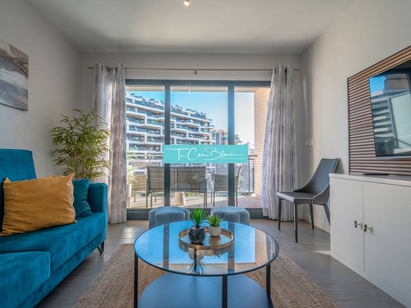 Luxusný byt  Alicante, 112m2, bazén, 2 garáže, posilňovňa - Obývacia izba v 2-izbovom byte s terasou, modrým gaučom a rastlinou.