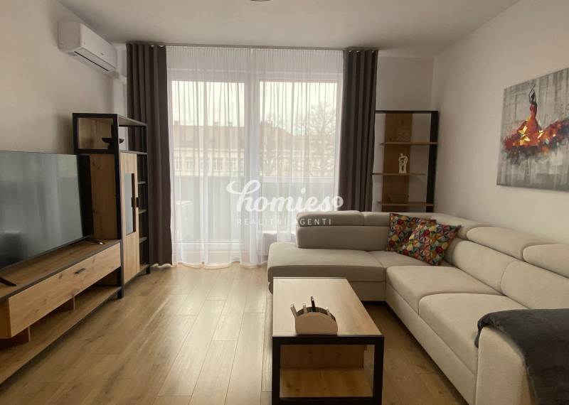 PRENÁJOM luxusný 2 izbový byt v centre mesta Nitra, parkovanie - Obývacia izba v 2-izbovom byte s podlahou s dreveným dekorom, svetlou sedačkou a televíziou.