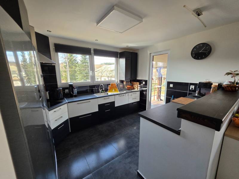 Zabehnutá novostavba: Komfort domu, pokoj vidieka a na skok do BB a ZV - Kuchyňa v rodinnom dome s keramickou podlahou, tmavým nábytkom a veľkými oknami.