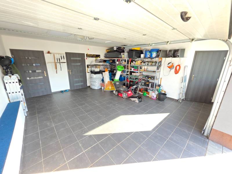 Zabehnutá novostavba: Komfort domu, pokoj vidieka a na skok do BB a ZV - Garáž v rodinnom dome s náradím a skladovacími policami, podlaha z keramických dlaždíc.