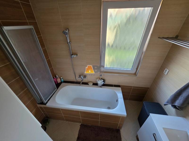 Zabehnutá novostavba: Komfort domu, pokoj vidieka a na skok do BB a ZV - Kúpeľňa v rodinnom dome s vaňou a oknom, obložená hnedými kachličkami.