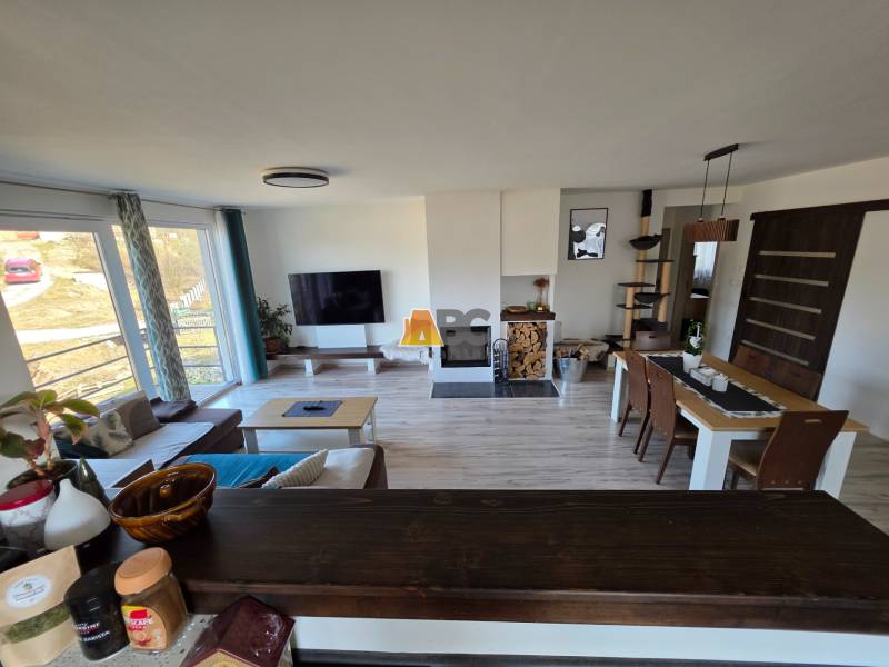 Zabehnutá novostavba: Komfort domu, pokoj vidieka a na skok do BB a ZV - Obývacia izba v rodinnom dome so sedačkou, televízorom a jedálenským stolom na podlahe s dreveným dekorom.