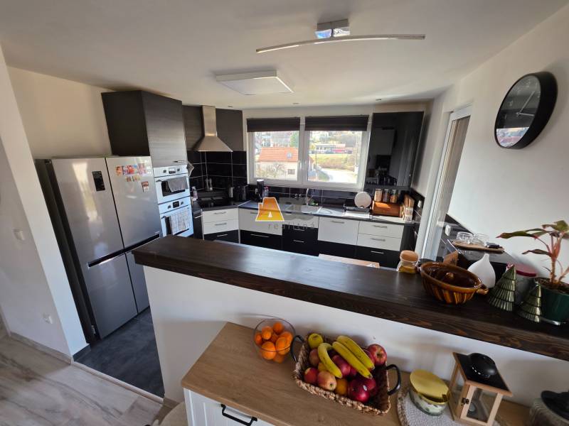 Zabehnutá novostavba: Komfort domu, pokoj vidieka a na skok do BB a ZV - Kuchyňa v rodinnom dome s modernými spotrebičmi, pultom a ovocím na stole.