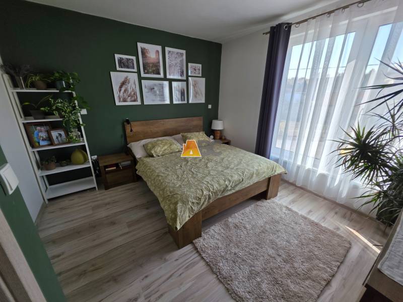 Zabehnutá novostavba: Komfort domu, pokoj vidieka a na skok do BB a ZV - Spálňa v rodinnom dome s podlahou s dreveným dekorom, zelenou stenou a kvetmi.