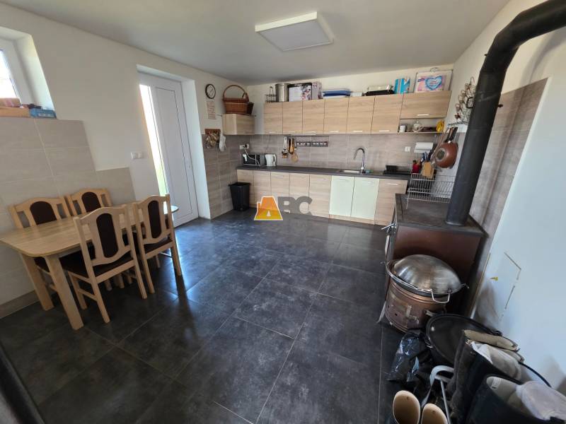 Zabehnutá novostavba: Komfort domu, pokoj vidieka a na skok do BB a ZV - Kuchyňa v rodinnom dome s kuchynskou linkou, jedálenským stolom a sporákom.