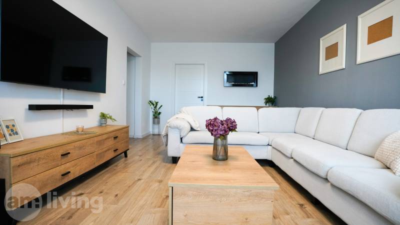 Rezervované -  3i byt v Nemšovej s loggiou po rekonštrukcii - 74m²  - Obývačka v 3-izbovom byte s bielym gaučom, podlahou s dreveným dekorom a dekoráciami.