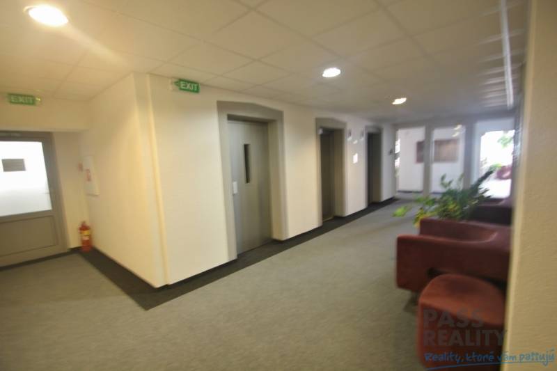 PRENÁJOM kancelárie 27 m2 - Technopol, Kutlíkova ul. - Interiér kancelárie s výťahmi a sedačkou, biela stena, piktogramy “EXIT”.
