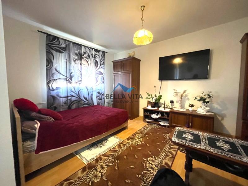 EXKLUZÍVNY PREDAJ - 1 izbový byt, Vodárenská ulica Galanta - Izba jedného bytu s posteľou, televízorom a podlahou s dreveným dekorom.