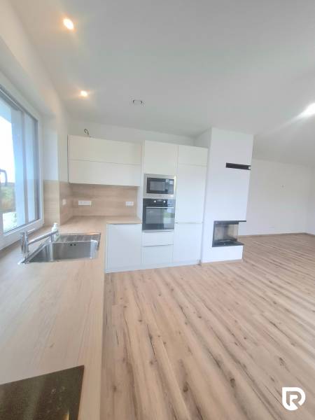 | 4 izbový rodinný dom s krbom a terasov | Slnečná | Ružindol - Biela kuchyňa s dreveným dekorom a vstavaným krbom v rodinnom dome.