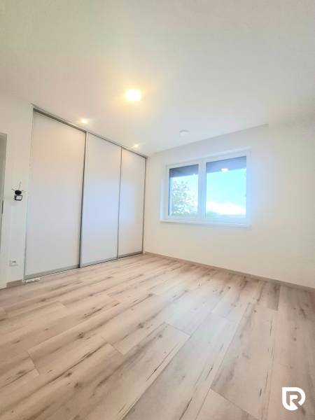 | 4 izbový rodinný dom s krbom a terasov | Slnečná | Ružindol - Izba s podlahou s dreveným dekorom, vstavanou skriňou a oknom v rodinnom dome.