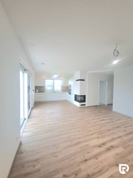 | 4 izbový rodinný dom s krbom a terasov | Slnečná | Ružindol - Obývacia izba v rodinnom dome s kuchyňou, krbom a podlahou s dreveným dekorom.