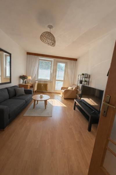 Predaj 3.izbového bytu v Ružinove v obkolesené borovicového lesíka - Obývacia izba v 3-izbovom byte s podlahou s dreveným dekorom a pohodlným nábytkom.