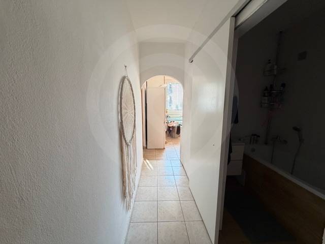 Predaj 3.izbového bytu v Ružinove v obkolesené borovicového lesíka - Chodba s dlažbou v 3-izbovom byte s dekoráciou na stene a pohľadom do kúpeľne.