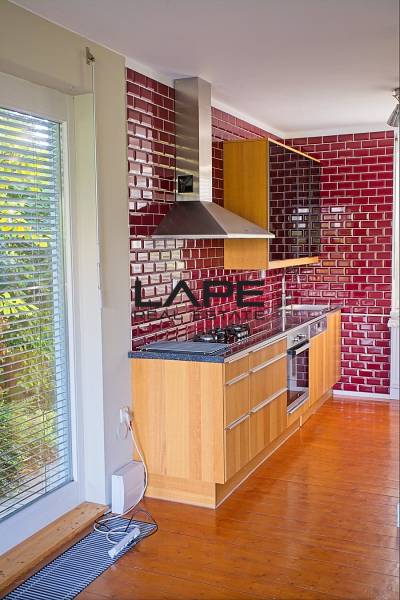 Rodinný dom s veľkou záhradou - Ružinov  - Kuchyňa v Rodinnom dome s červenými obkladmi, drevenými skrinkami a podlahou s dreveným dekorom.