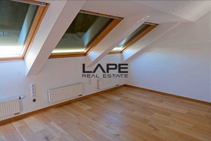 Rodinný dom s veľkou záhradou - Ružinov  - Podkrovie s veľkými oknami a podlahou s dreveným dekorom v rodinnom dome.