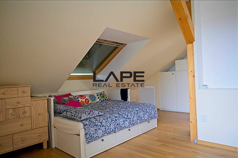 Rodinný dom s veľkou záhradou - Ružinov  - Podkrovná spálňa v rodinnom dome s posteľou, komodou, strešným oknom a podlahou s dreveným dekorom.