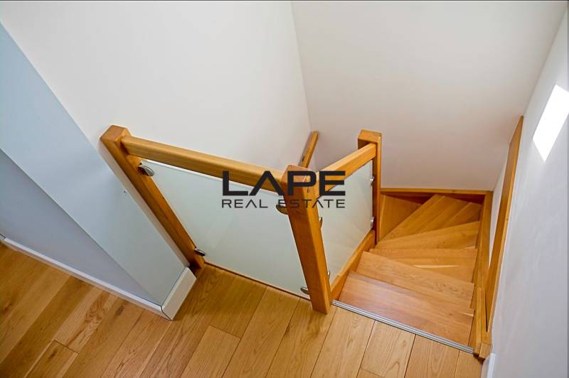 Rodinný dom s veľkou záhradou - Ružinov  - Drevené schodisko so skleneným zábradlím v rodinnom dome s podlahou s dreveným dekorom.