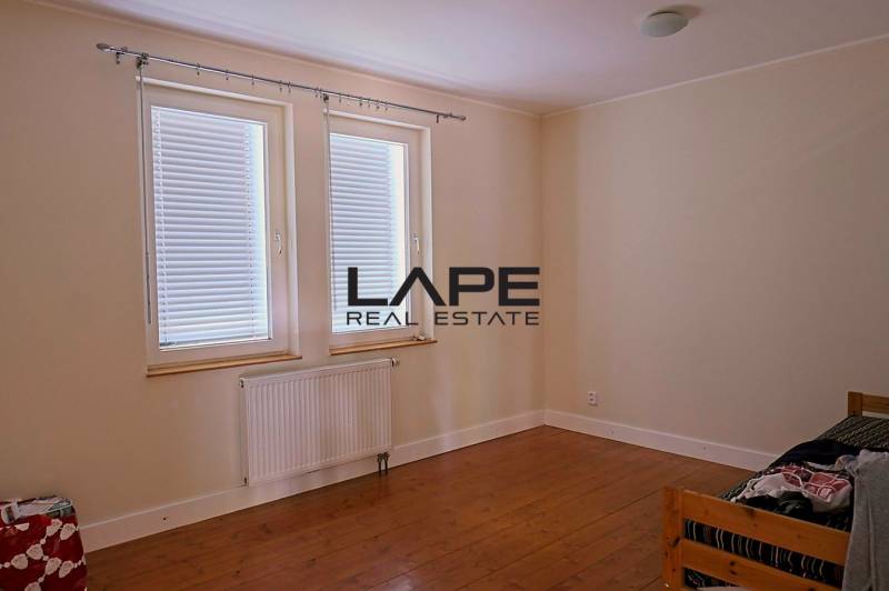 Rodinný dom s veľkou záhradou - Ružinov  - Izba v rodinnom dome, béžové steny, podlaha s dreveným dekorom, dve okná s roletami.