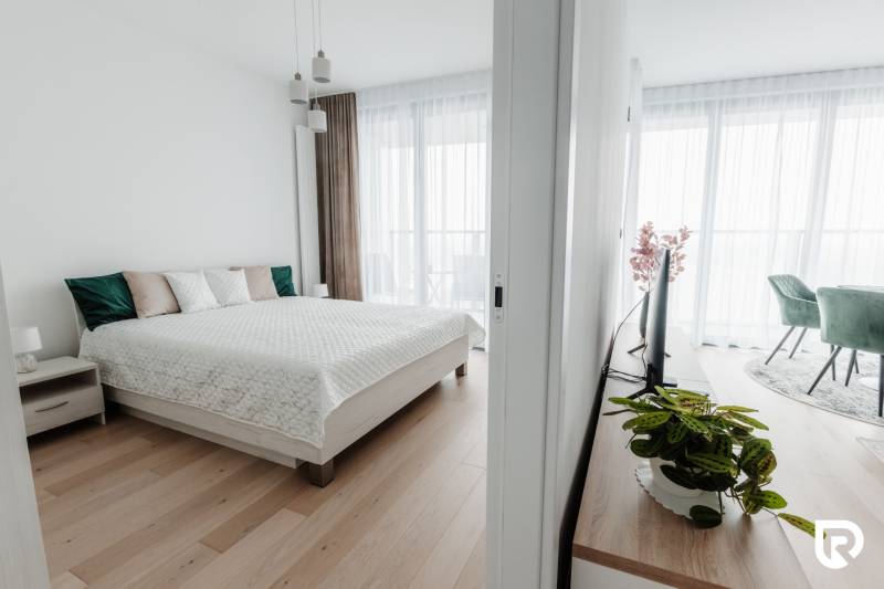 | E2Tower | 20.poschodie | 2i byt | panoramatický výhľad |  - Svetlá spálňa v 2-izbovom byte s posteľou a podlahou s dreveným dekorom.