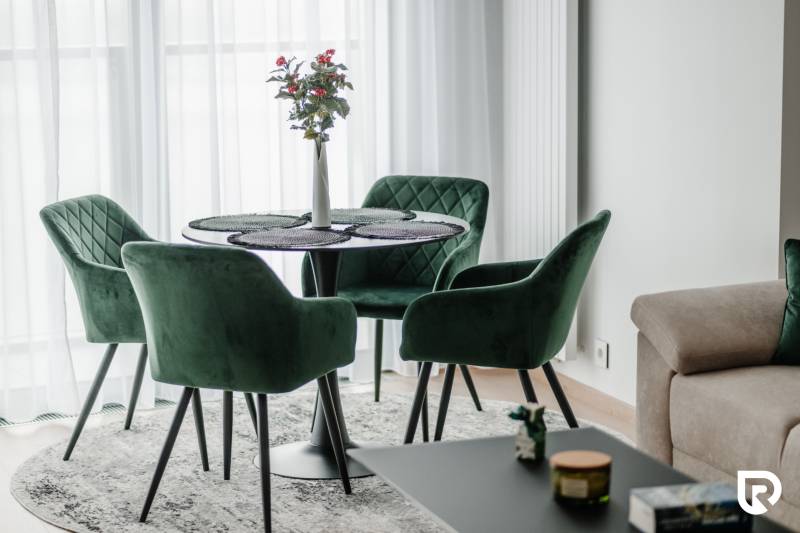 | E2Tower | 20.poschodie | 2i byt | panoramatický výhľad |  - Zelené kreslá a stôl s kvetom v 2-izbovom byte na podlahe s dreveným dekorom.