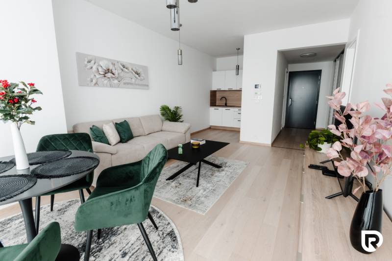 | E2Tower | 20.poschodie | 2i byt | panoramatický výhľad |  - Obývacia izba v 2-izbovom byte s podlahou s dreveným dekorom, vankúše a rastliny.