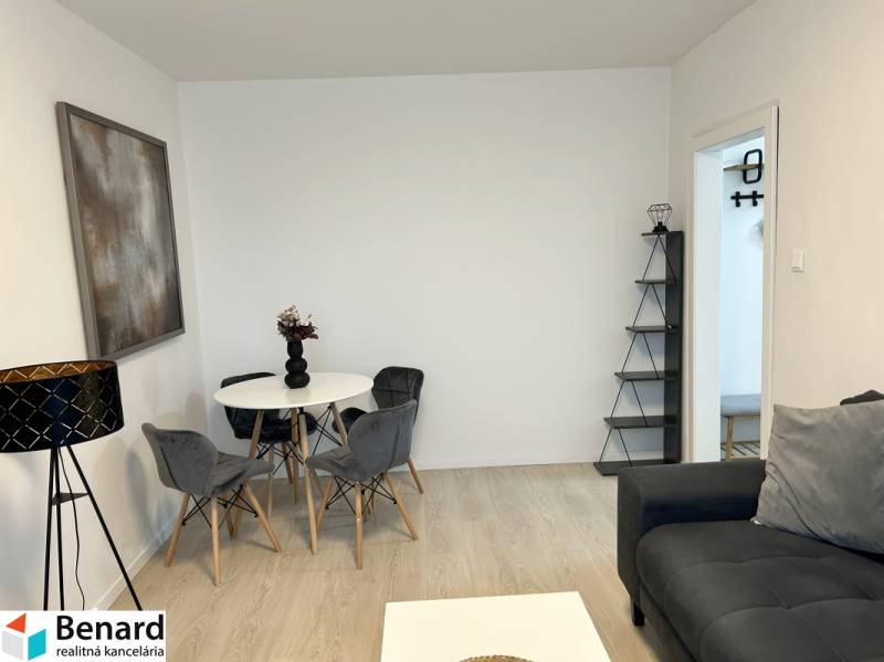 NA PREDAJ ŠTÝLOVÝ 2- IZBOVÝ BYT, 50m2, SÍDLISKO 2, PREŠOV - Obývačka v 2-izbovom byte s podlahou s dreveným dekorom, sivou sedačkou a jedálenským stolom.