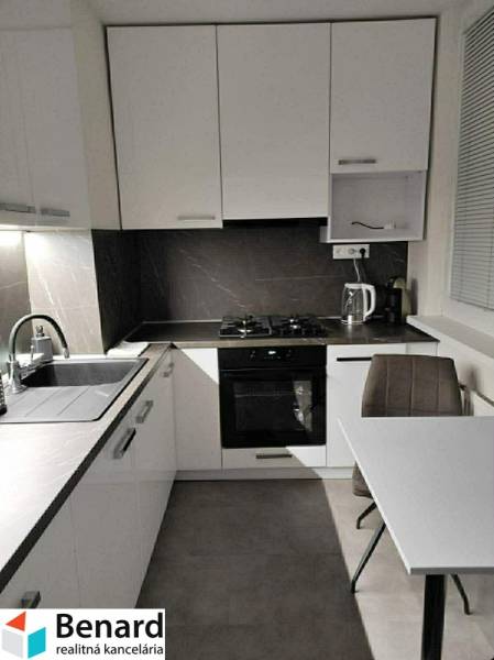 NA PREDAJ ŠTÝLOVÝ 2- IZBOVÝ BYT, 50m2, SÍDLISKO 2, PREŠOV - Kuchyňa s bielymi skrinkami a stolom v 2-izbovom byte s podlahou s dreveným dekorom.