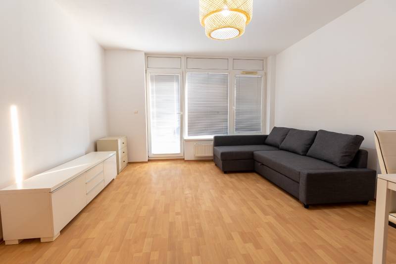 Luxusný 2-izbový byt + 2 balkóny, 73 m², garážové státie, Ružinov - Obývacia izba v 2-izbovom byte s pohovkou, skrinkou a podlahou s dreveným dekorom.