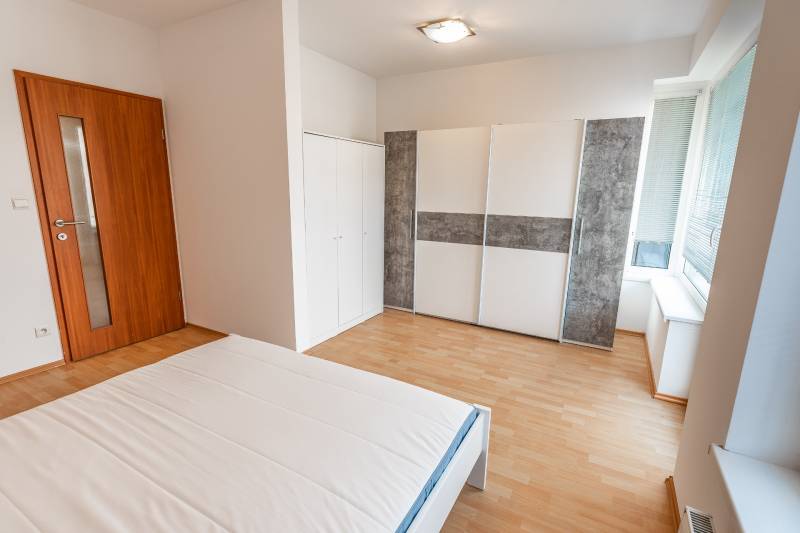 Luxusný 2-izbový byt + 2 balkóny, 73 m², garážové státie, Ružinov - Spálňa s posteľou, šatníkovou skriňou a podlahou s dreveným dekorom v 2-izbovom byte.