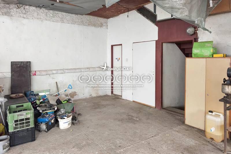 4-izbový podkrovný byt s nebytovým priestorom v obci Pavlice - Garáž v rodinnom dome, odložené náradie, betónová podlaha, schody a biely nábytok.