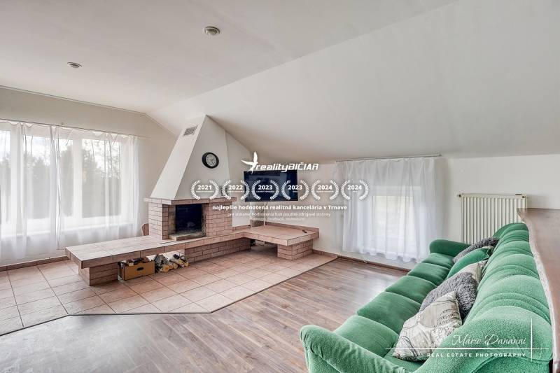 4-izbový podkrovný byt s nebytovým priestorom v obci Pavlice - Obývačka s krbom, zelenou pohovkou a podlahou s dreveným dekorom v rodinnom dome.