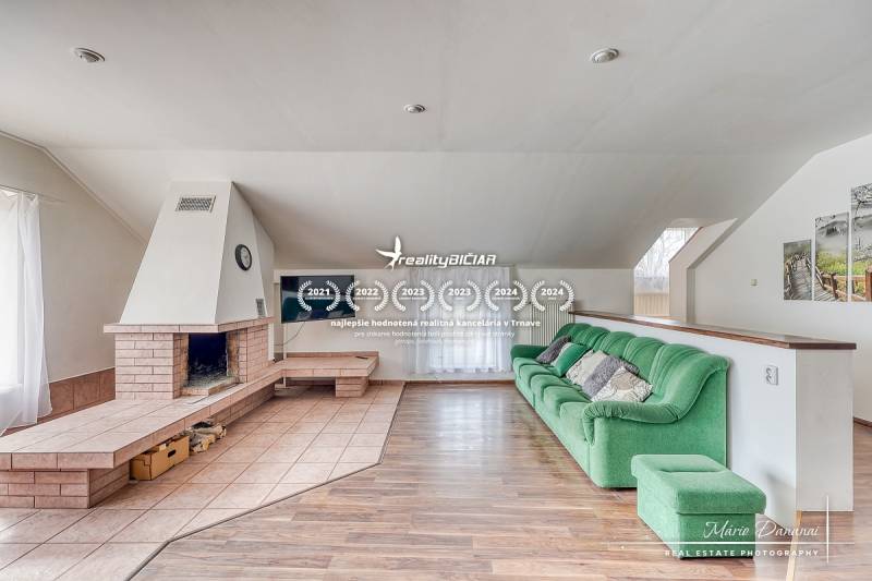 4-izbový podkrovný byt s nebytovým priestorom v obci Pavlice - Obývačka v rodinnom dome s krbom, zelenou sedačkou a podlahou s dreveným dekorom.