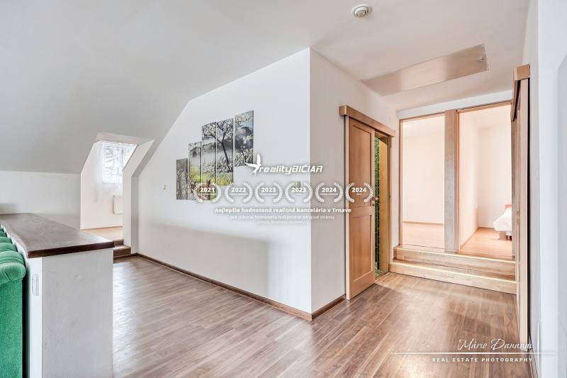 4-izbový podkrovný byt s nebytovým priestorom v obci Pavlice - Interiér rodinného domu so schodmi, dreveným dekorom podlahy a obrazom na stene.