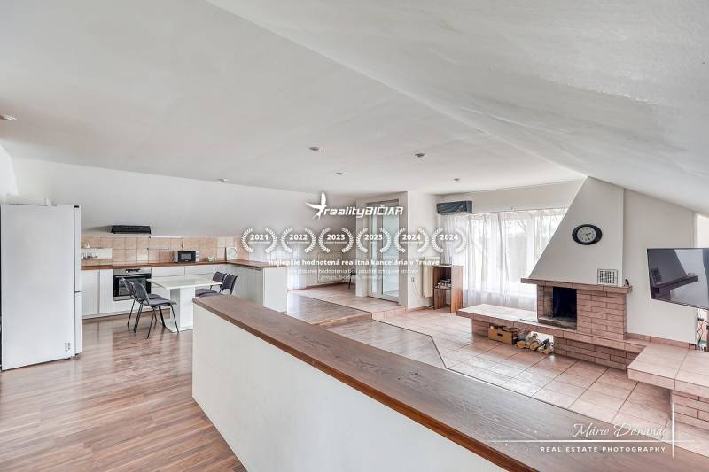 4-izbový podkrovný byt s nebytovým priestorom v obci Pavlice - Obývacia izba s krbom a kuchynskou časťou, podlaha s dreveným dekorom, svetlá miestnosť.