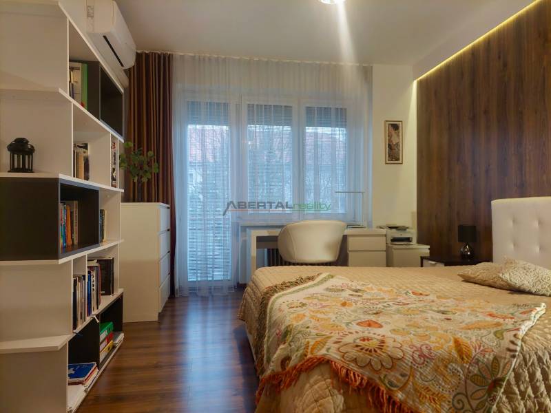 Vkusný, moderný 2 izb, klíma, 870 s ener., Sibírska ul./Nové Mesto - Spálňa v 2-izbovom byte s podlahou s dreveným dekorom, knižnica a písací stôl.