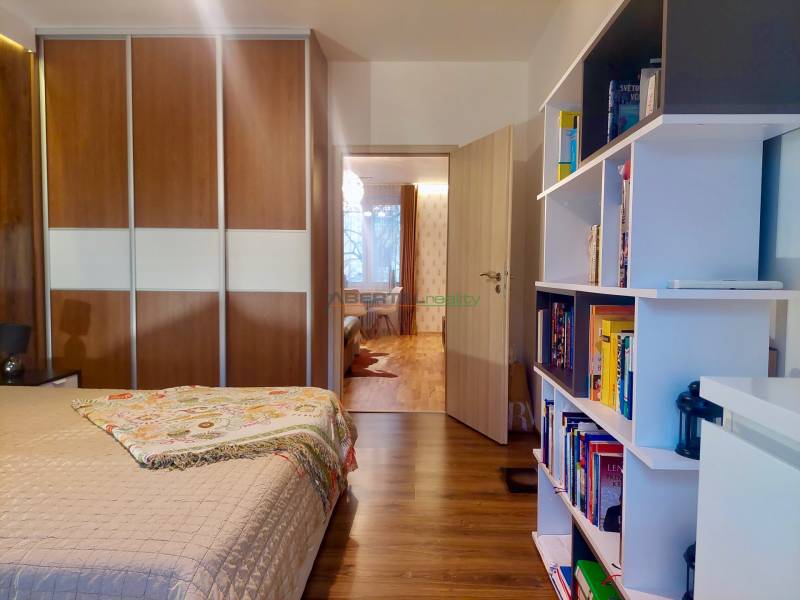 Vkusný, moderný 2 izb, klíma, 870 s ener., Sibírska ul./Nové Mesto - Spálňa v 2-izbovom byte s podlahou s dreveným dekorom, vstavanou skriňou a knižnicou.