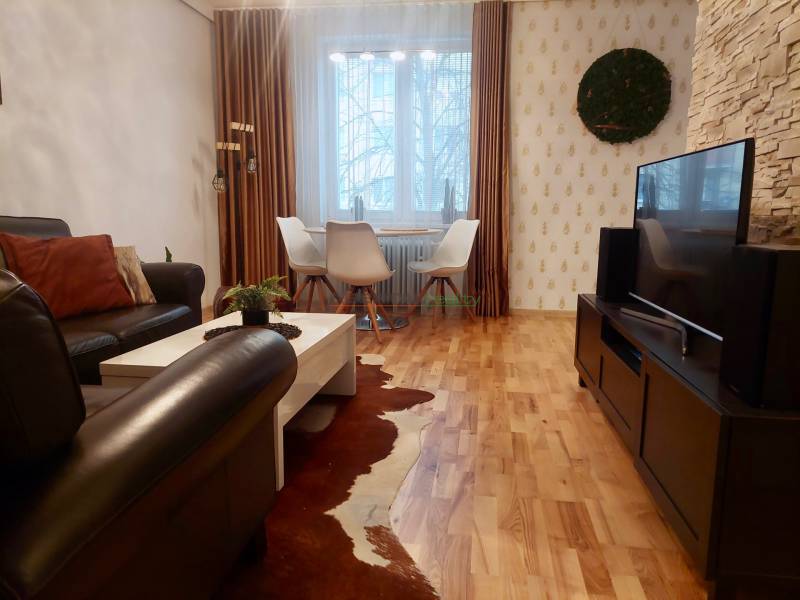 Vkusný, moderný 2 izb, klíma, 870 s ener., Sibírska ul./Nové Mesto - Obývačka v 2-izbovom byte s podlahou s dreveným dekorom, pohodlnou sedačkou a televíziou.