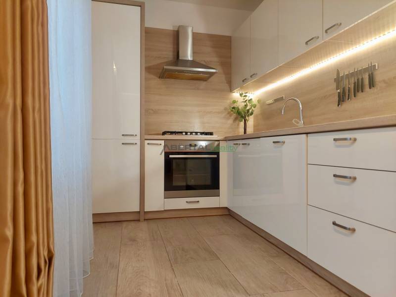 Vkusný, moderný 2 izb, klíma, 870 s ener., Sibírska ul./Nové Mesto - Kuchynská linka v 2-izbovom byte s podlahou v drevenom dekore a závesmi.