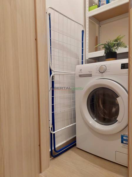 Vkusný, moderný 2 izb, klíma, 870 s ener., Sibírska ul./Nové Mesto - Práčka v kúpeľni 2-izbového bytu, vedľa sušiak a police s dekoráciou.