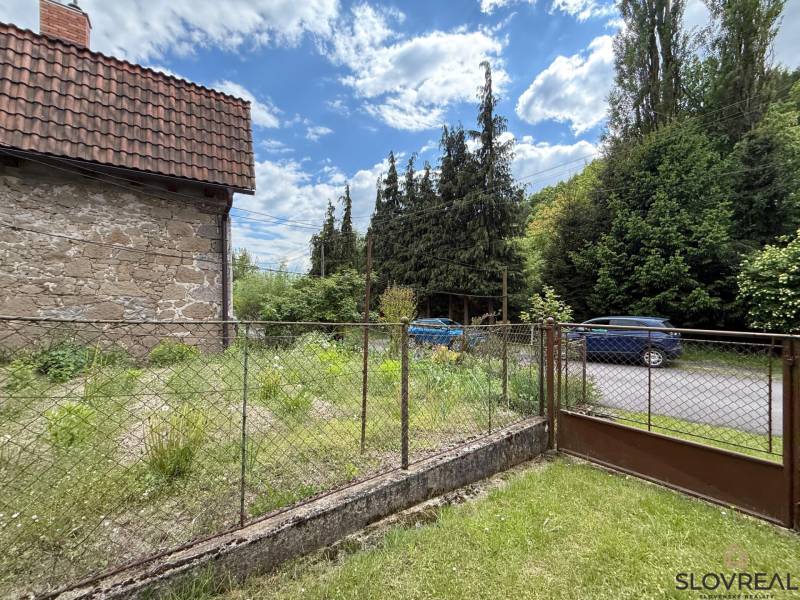 Predaj domu v Janovej Lehote - Kamenná stena rodinného domu v Janovej Lehote, pri ceste s autami a zeleňou.