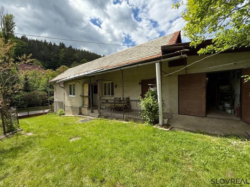 Predaj domu v Janovej Lehote - Rodinný dom v Janovej Lehote so záhradou a lesom v pozadí pod oblačnou oblohou.