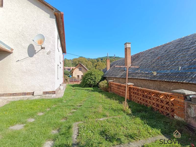 : Predaj rodinného domu s veľkým pozemkom v obci Pitelová  - Exteriér rodinného domu v Pitelovej so satelitom, trávnikom a tehlovým plotom.