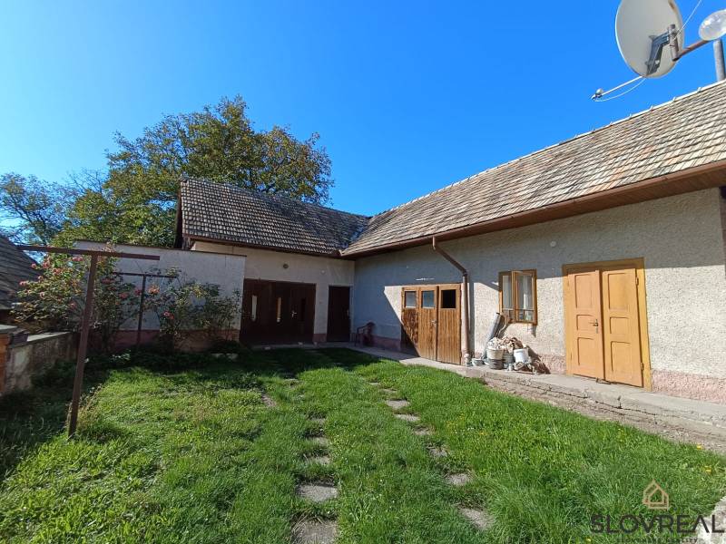 : Predaj rodinného domu s veľkým pozemkom v obci Pitelová  - Rodinný dom v Pitelovej s drevenou strechou a zelenou záhradou.