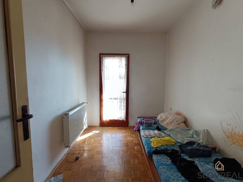 : Predaj rodinného domu s veľkým pozemkom v obci Pitelová  - Izba v rodinnom dome s radiátorom, jednoduchým lôžkom a podlahou s dreveným dekorom.